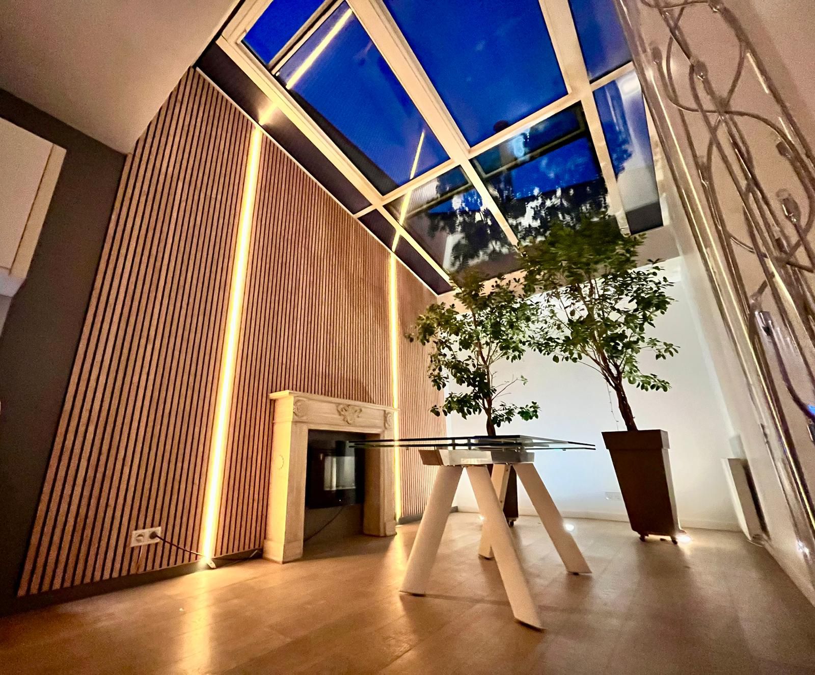 Salon en double hauteur sous verrière, mur en lattes de bois rétroéclairé et cheminée en marbre — réalisation AMELA Concept